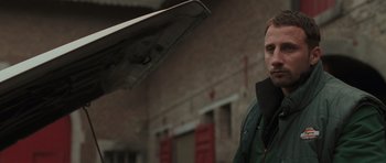 Movie still from “Bullhead” (2011), directed by Michaël R. Roskam – A man standing in front of a brick building; Close Up shot, Over the shoulder angle