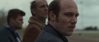 Movie still from “Bullhead” (2011), directed by Michaël R. Roskam – Two men standing next to each other in front of a building; Close Up shot, Over the shoulder angle