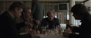 Movie still from “Bullhead” (2011), directed by Michaël R. Roskam – A group of people sitting at a table with drinks; Medium shot, Over the shoulder angle