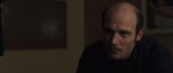Movie still from “Bullhead” (2011), directed by Michaël R. Roskam – A man with a bald head is sitting in a dark room; Close Up shot, Over the shoulder angle