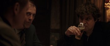 Movie still from “Bullhead” (2011), directed by Michaël R. Roskam – Two people sitting at a table in a dark room; Close Up shot, Over the shoulder angle