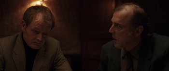 Movie still from “Bullhead” (2011), directed by Michaël R. Roskam – Two people sitting at a table in front of each other; Close Up shot, Over the shoulder angle