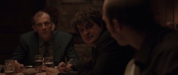 Movie still from “Bullhead” (2011), directed by Michaël R. Roskam – A man sitting at a table with other people; Medium shot, Over the shoulder angle