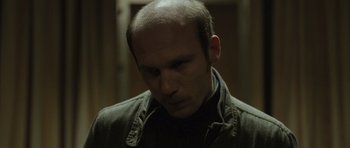 Movie still from “Bullhead” (2011), directed by Michaël R. Roskam – A man with a bald head looking to his left; Close Up shot, Over the shoulder angle