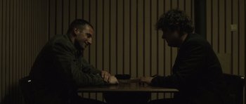 Movie still from “Bullhead” (2011), directed by Michaël R. Roskam – Two men sitting at a table playing a game of chess; Medium shot, Over the shoulder angle