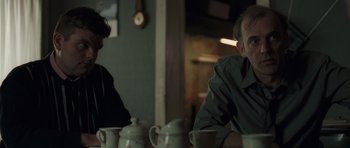 Movie still from “Bullhead” (2011), directed by Michaël R. Roskam – Two people sitting at a table with tea pots; Medium shot, Over the shoulder angle