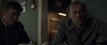 Movie still from “Bullhead” (2011), directed by Michaël R. Roskam – A person sitting on a couch in a living room; Close Up shot, Over the shoulder angle