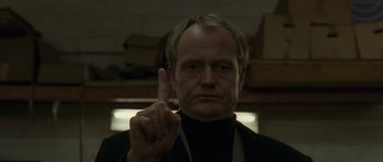 Movie still from “Bullhead” (2011), directed by Michaël R. Roskam – A man in a black shirt is holding up a finger; Close Up shot, Low angle