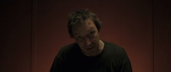 Movie still from “Bullhead” (2011), directed by Michaël R. Roskam – A man in a black t - shirt is looking at the camera; Close Up shot, Low angle
