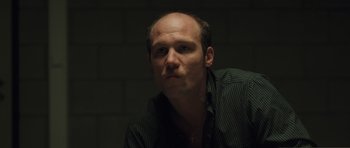 Movie still from “Bullhead” (2011), directed by Michaël R. Roskam – A man with a bald head is sitting in a dark room; Close Up shot, Low angle