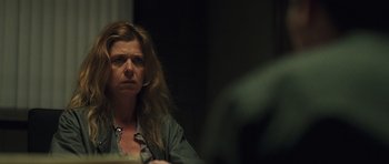 Movie still from “Bullhead” (2011), directed by Michaël R. Roskam – A woman sitting in front of a table looking at the camera; Close Up shot, Over the shoulder angle