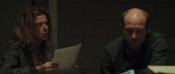 Movie still from “Bullhead” (2011), directed by Michaël R. Roskam – A man and a woman sitting in front of each other holding papers; Close Up shot, Over the shoulder angle