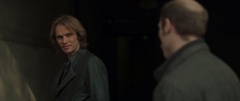 Movie still from “Bullhead” (2011), directed by Michaël R. Roskam – A man standing next to another man in a dark room; Close Up shot, Over the shoulder angle