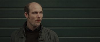 Movie still from “Bullhead” (2011), directed by Michaël R. Roskam – A man with a bald head is looking to his left; Close Up shot, Over the shoulder angle