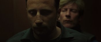 Movie still from “Bullhead” (2011), directed by Michaël R. Roskam – A man is looking down at his face while another man looks on in the background; Close Up shot, Low angle