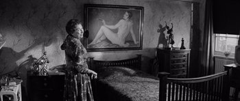 Movie still from “Bunny Lake Is Missing” (1965), directed by Otto Preminger – An older woman standing in front of a painting of a naked woman; Medium shot, Over the shoulder angle