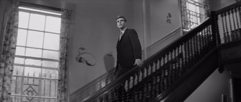 Movie still from “Bunny Lake Is Missing” (1965), directed by Otto Preminger – A black and white photo of a man in a suit on a staircase; Medium shot, Low angle