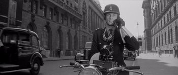 Movie still from “Bunny Lake Is Missing” (1965), directed by Otto Preminger – A man in a uniform sitting on the back of a motorcycle; Medium shot, Low angle