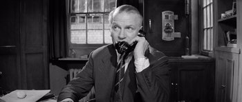 Movie still from “Bunny Lake Is Missing” (1965), directed by Otto Preminger – An older man talking on a phone while sitting in a chair; Close Up shot, High angle