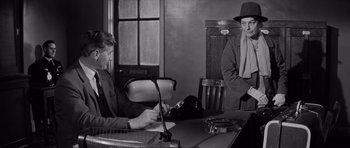 Movie still from “Bunny Lake Is Missing” (1965), directed by Otto Preminger – Two men are sitting at a desk in an office; Medium shot, Over the shoulder angle