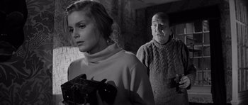 Movie still from “Bunny Lake Is Missing” (1965), directed by Otto Preminger – A man and a woman holding guns in front of a window; Medium shot, Low angle