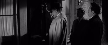 Movie still from “Bunny Lake Is Missing” (1965), directed by Otto Preminger – A black and white photo of a man in a hat; Medium shot, Low angle