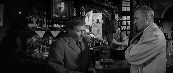 Movie still from “Bunny Lake Is Missing” (1965), directed by Otto Preminger – A man sitting at a table in front of two other men; Medium shot, Over the shoulder angle