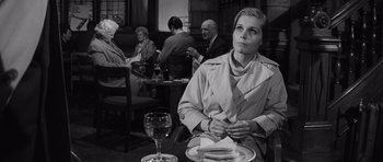 Movie still from “Bunny Lake Is Missing” (1965), directed by Otto Preminger – A black and white photo of a woman sitting at a table; Medium shot, Over the shoulder angle