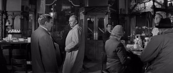 Movie still from “Bunny Lake Is Missing” (1965), directed by Otto Preminger – A group of people sitting at a table in front of a building; Medium shot, Over the shoulder angle