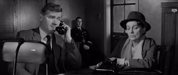 Movie still from “Bunny Lake Is Missing” (1965), directed by Otto Preminger – A man talking on a phone while another man watches; Medium shot, Over the shoulder angle