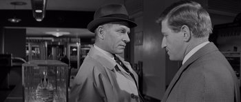 Movie still from “Bunny Lake Is Missing” (1965), directed by Otto Preminger – A man wearing a hat and a trench coat talking to another man in a suit; Close Up shot, Over the shoulder angle