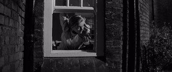 Movie still from “Bunny Lake Is Missing” (1965), directed by Otto Preminger – A black and white photo of a woman taking a picture through a window; Medium shot, Low angle