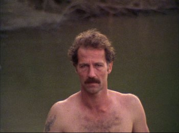 Movie still from “Burden of Dreams” (1982), directed by Les Blank – A man with a beard and a mustache is standing in front of a body of water; Close Up shot, High angle