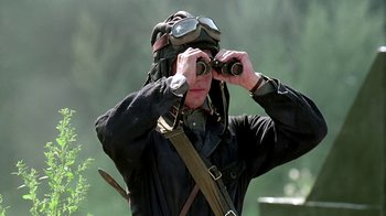 Movie still from “Burnt by the Sun” (1994), directed by Nikita Mikhalkov – A man in a black jacket and goggles looking through binoculars; Close Up shot, Over the shoulder angle