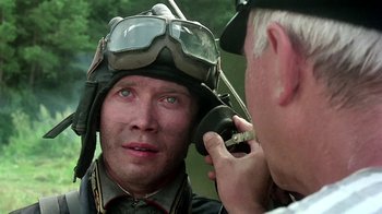 Movie still from “Burnt by the Sun” (1994), directed by Nikita Mikhalkov – A man wearing a helmet while another man adjusts his ear piece; Close Up shot, Over the shoulder angle