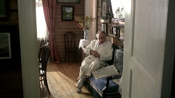 Movie still from “Burnt by the Sun” (1994), directed by Nikita Mikhalkov – An older man sitting on a chair in a room; Wide shot, High angle