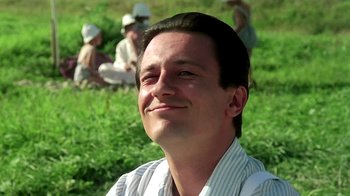 Movie still from “Burnt by the Sun” (1994), directed by Nikita Mikhalkov – A man smiling while sitting in front of a group of people; Close Up shot, Low angle