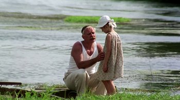 Movie still from “Burnt by the Sun” (1994), directed by Nikita Mikhalkov – An older man and a young girl by a body of water; Medium shot, Over the shoulder angle