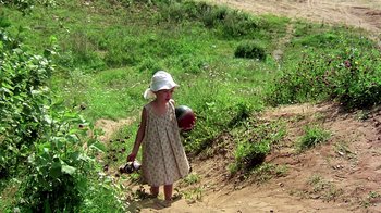 Movie still from “Burnt by the Sun” (1994), directed by Nikita Mikhalkov – A little girl in a dress and a white hat is holding a ball; Wide shot, High angle