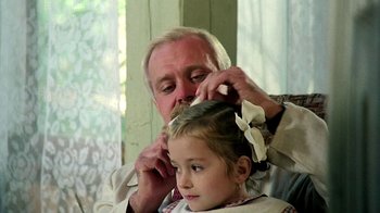 Movie still from “Burnt by the Sun” (1994), directed by Nikita Mikhalkov – An older man is cutting a young girl's hair; Close Up shot, Over the shoulder angle