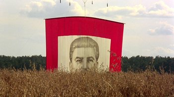 Movie still from “Burnt by the Sun” (1994), directed by Nikita Mikhalkov – A large mural of a man's face in a field of grass; Extreme Wide shot, Low angle