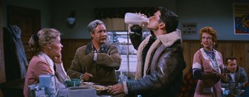 Movie still from “Bus Stop” (1956), directed by Joshua Logan – A man drinking milk from a bottle while another man looks on; Medium shot, Over the shoulder angle