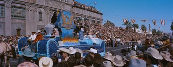 Movie still from “Bus Stop” (1956), directed by Joshua Logan – A crowd of people gathered around a parade float; Extreme Wide shot, High angle