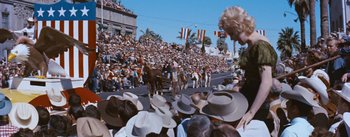 Movie still from “Bus Stop” (1956), directed by Joshua Logan – A crowd of people watching a parade on a city street; Wide shot, Low angle