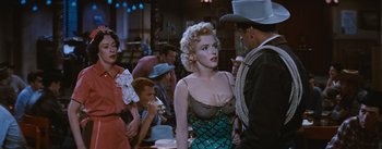 Movie still from “Bus Stop” (1956), directed by Joshua Logan – A woman in a green dress standing next to a man in a cowboy hat; Medium shot, Over the shoulder angle