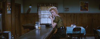 Movie still from “Bus Stop” (1956), directed by Joshua Logan – A woman sitting at a table with a glass of beer; Medium shot, Low angle