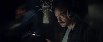 A man wearing headphones and looking at a cell phone in front of a microphone