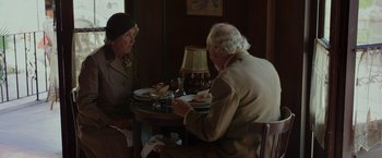 Movie still from “By the Sea” (2015), directed by Angelina Jolie – An older man and woman sitting at a dinner table; Medium shot, Over the shoulder angle