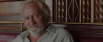 Movie still from “By the Sea” (2015), directed by Angelina Jolie – An older man with white hair and a white beard; Close Up shot, Over the shoulder angle