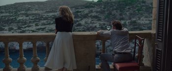 Movie still from “By the Sea” (2015), directed by Angelina Jolie – A man and a woman sitting on a balcony drinking a glass of white wine; Wide shot, Over the shoulder angle